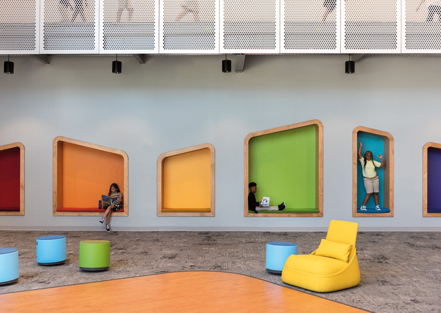 Children interact in colorful alcoves within a spacious area, featuring seating and a contemporary design. Soft seating and playful colors enhance the environment.